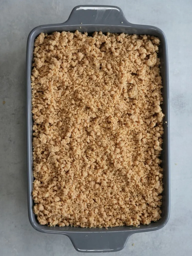 crumble sprinkled on top of peeled apples in oven dish
