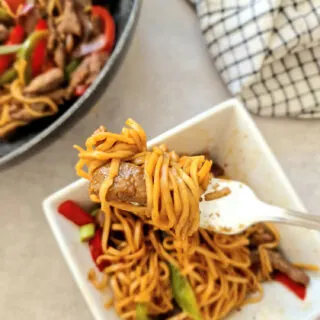 stir fry beef and noodles on a fork above bowl and wok