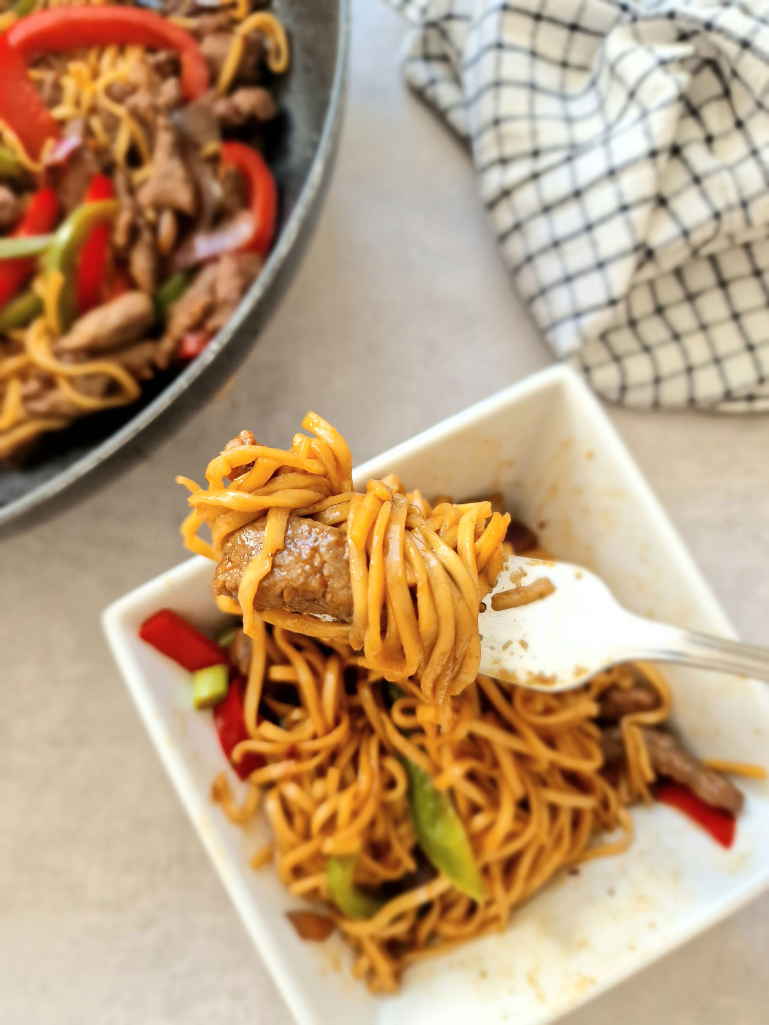 stir fry beef and noodles on a fork above bowl and wok