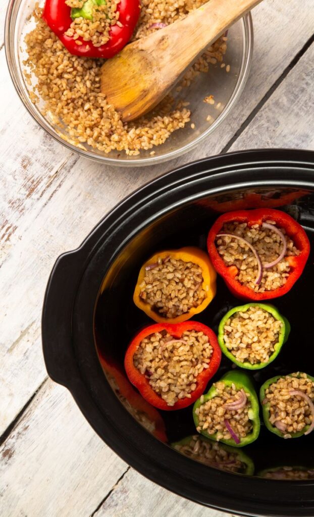 stuffed peppers standing upright in the slow cooker with cooked rice, chilli and onions inside them.