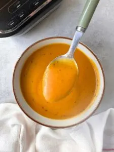 butternut squash and sweet potato soup in a bowl with a spoon held above it