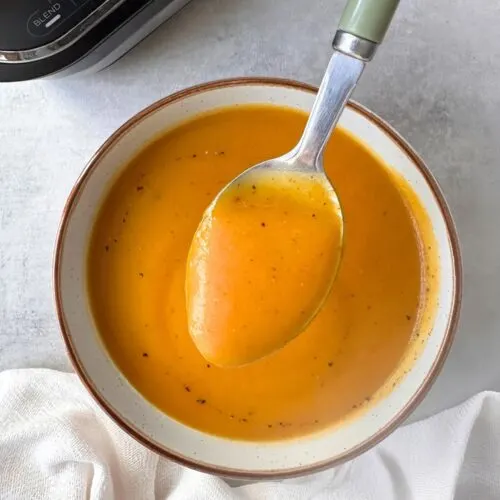 butternut squash and sweet potato soup in a bowl with a spoon held above it