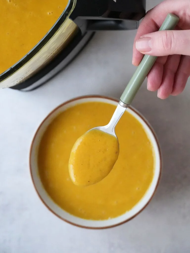 sweet potato and chickpea soup cooked in a bowl with a spoon above it. part of the ninja soup maker jug is shown in the corner