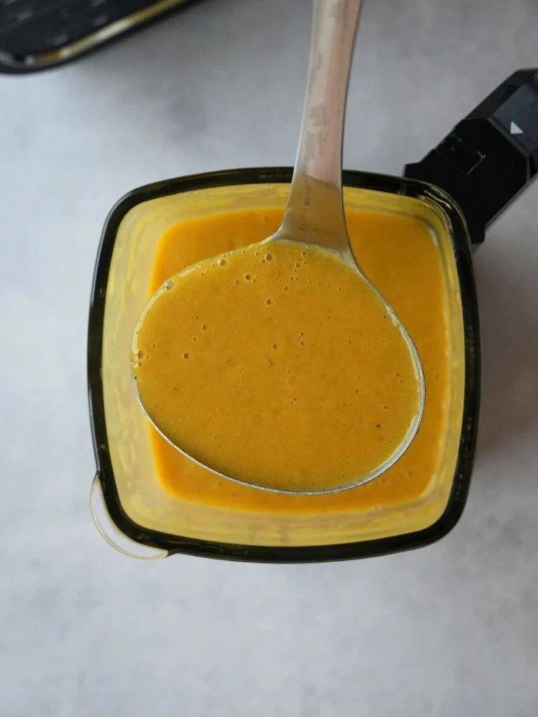 ninja soup maker with soup cooked inside with a serving spoon with the soup in it