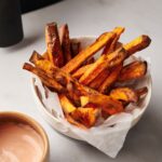 sweet potato fries in bowl next to sauce and air fryer