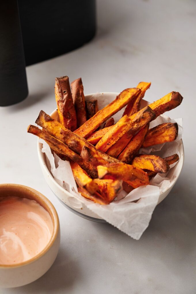 sweet potato fries in bowl next to sauce and air fryer