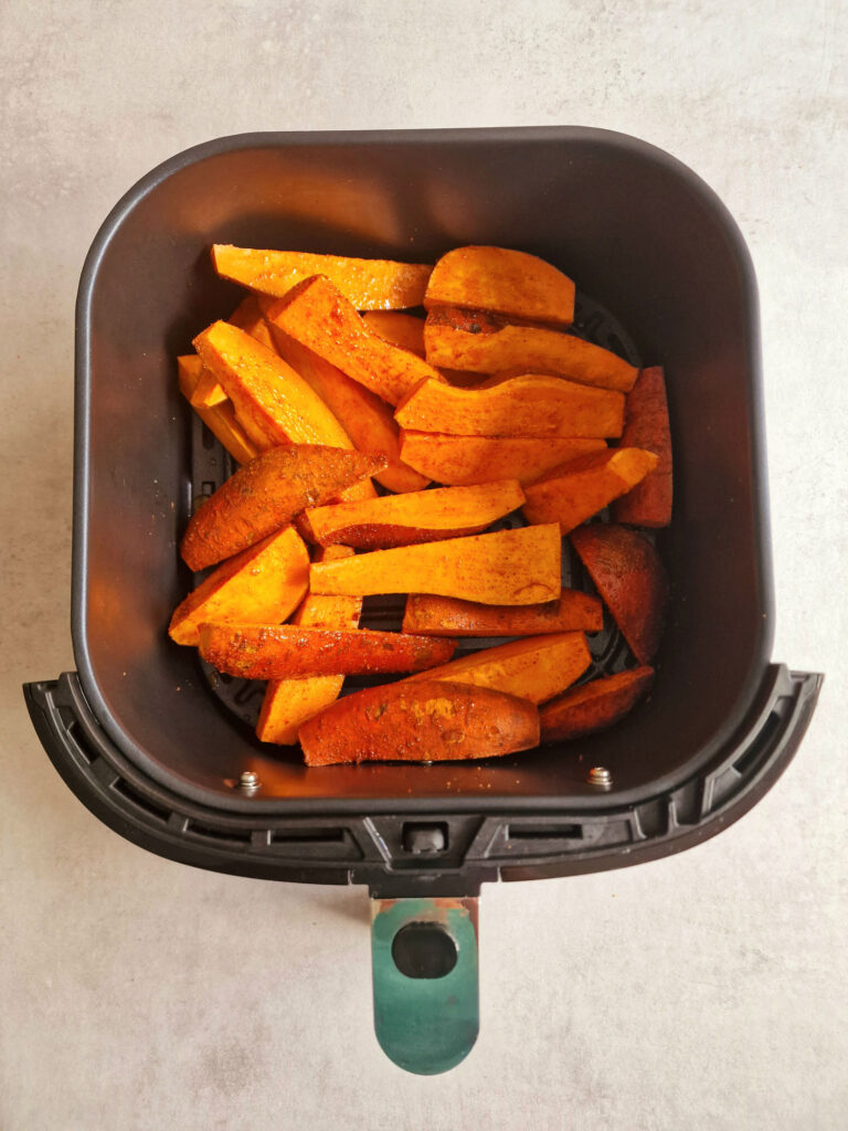 raw sweet potato wedges in an air fryer basket
