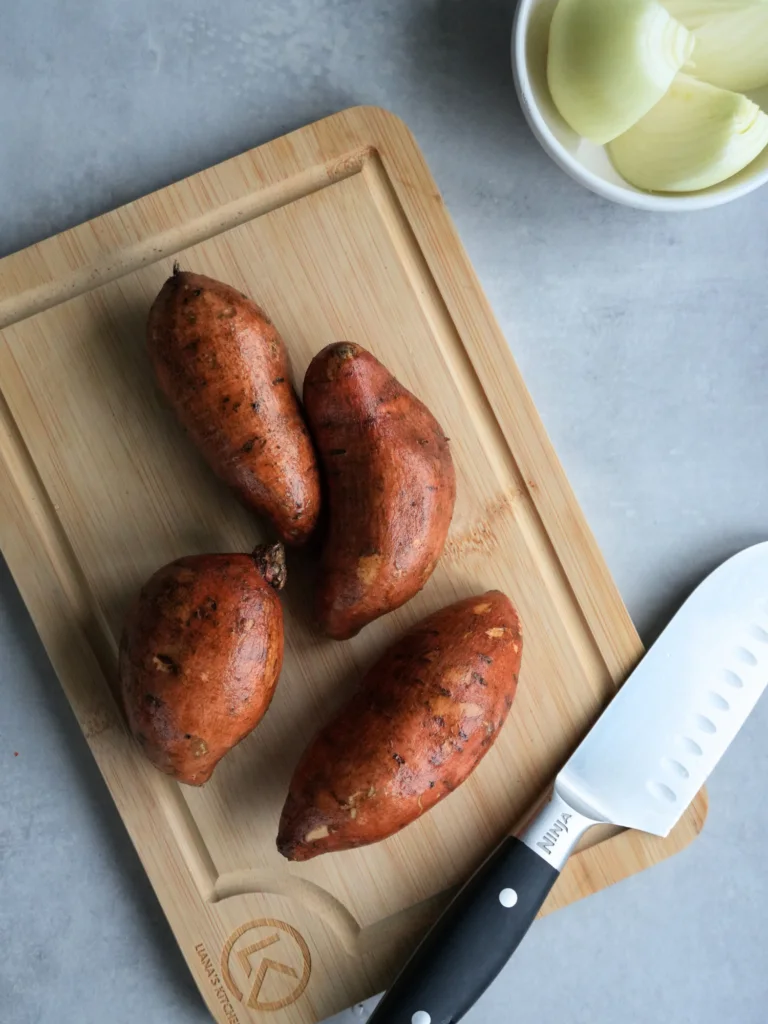 4 sweet potatoes on a chopping board with a Ninja knife next to it