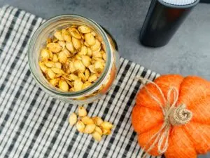 air fried pumpkin seeds in a jar next to an air fryer and a pumpkin