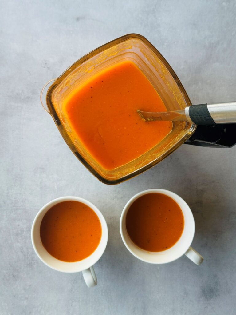 tomato and red pepper soup in a ninja soup maker with two cups of soup next to it
