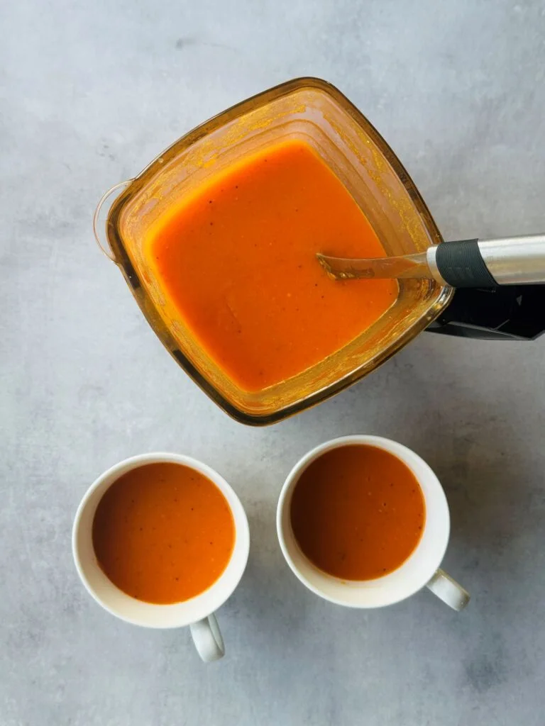 tomato and red pepper soup in a ninja soup maker with two cups of soup next to it
