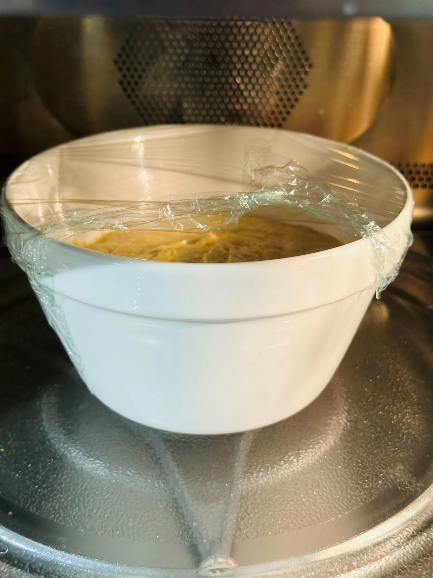 sponge pudding with cling film over it in a bowl placed in a microwave