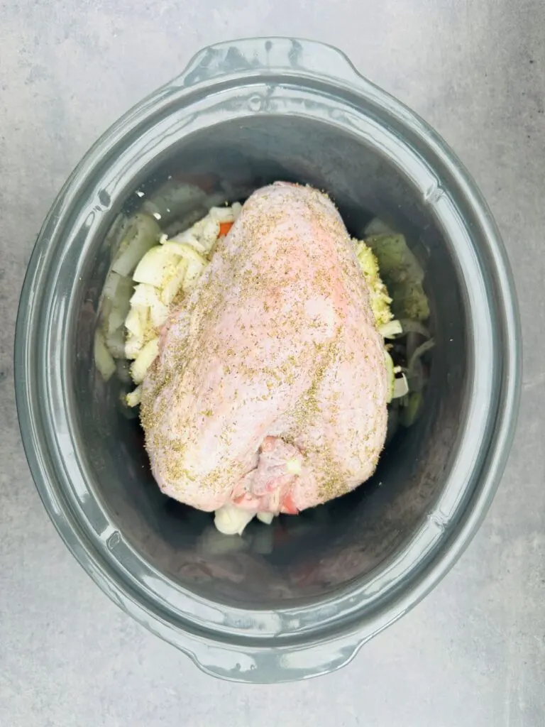 seasoned turkey crown with onions and carrots in slow cooker