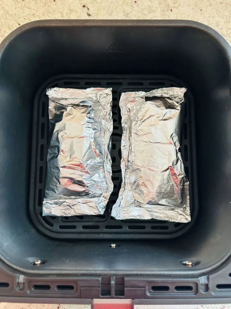 two chicken breasts wrapped in foil in an air fryer basket