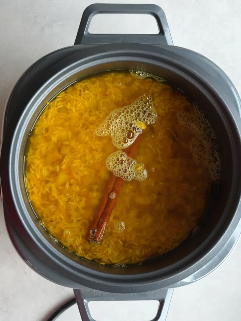 basmati rice, spices and water in a rice cooker with the lid off