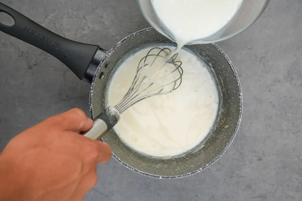 whisking milk into white sauce in saucepan