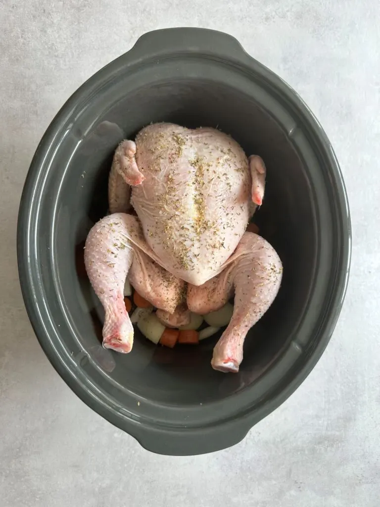 whole chicken in slow cooker with herbs on top of carrots and onions